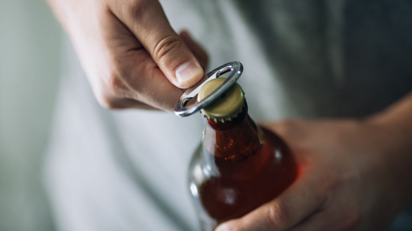 Eine Bierflasche wird mit einem Flaschenöffner geöffnet.