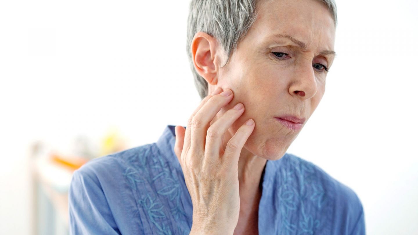 Canker sores: woman holding her right cheek with one hand and grimacing. Her mouth is shut.