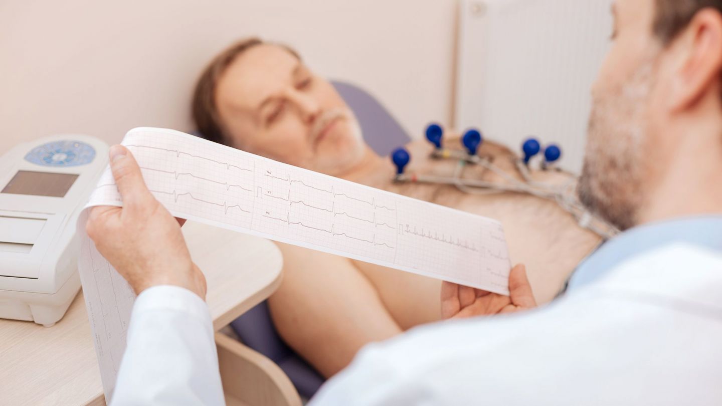 AV bloğu: Doktor EKG sonuçlarını inceliyor, hasta muayene masasında yatıyor.