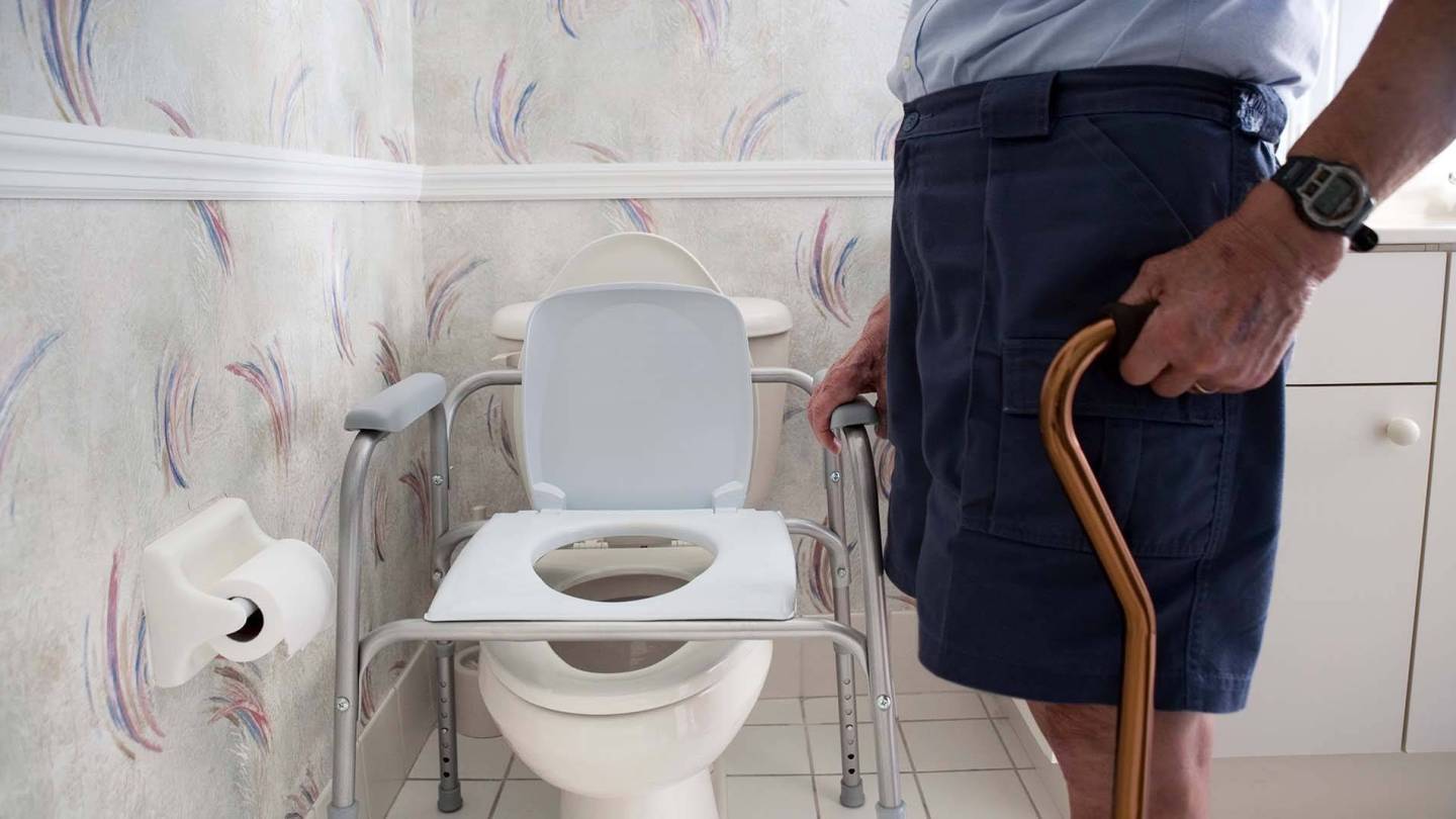 رجل يُمسك عكازًا أمام مرحاض مناسب لذوي الإعاقات