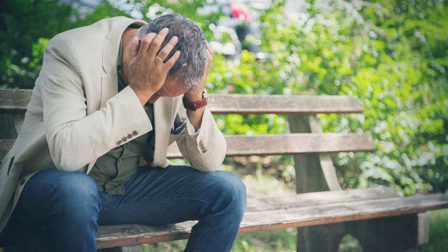 Küme tipi baş ağrısı: Bir adam bir bankta oturuyor ve başını eğiyor ve iki eliyle şakaklarını tutuyor.