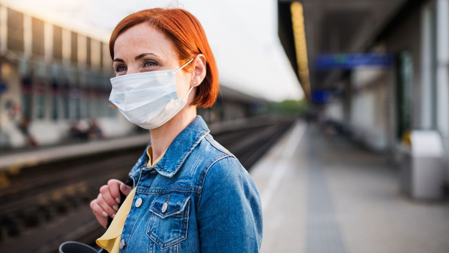 Eine Frau steht an einem Bahnsteig und trägt eine Mund-Nasen-Schutzmaske. 
