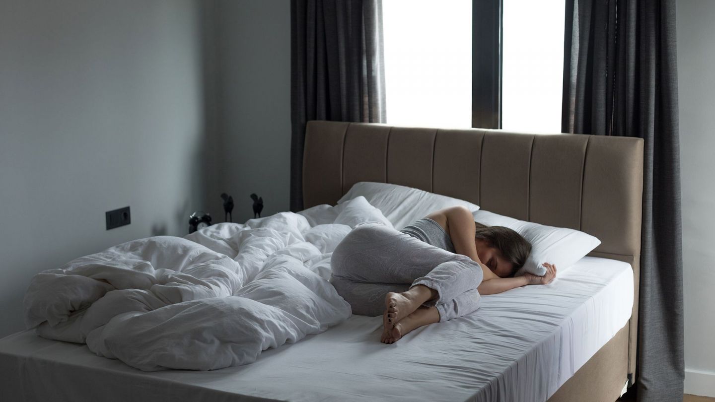 Депрессия: женщина лежит на большой кровати, свернувшись калачиком.