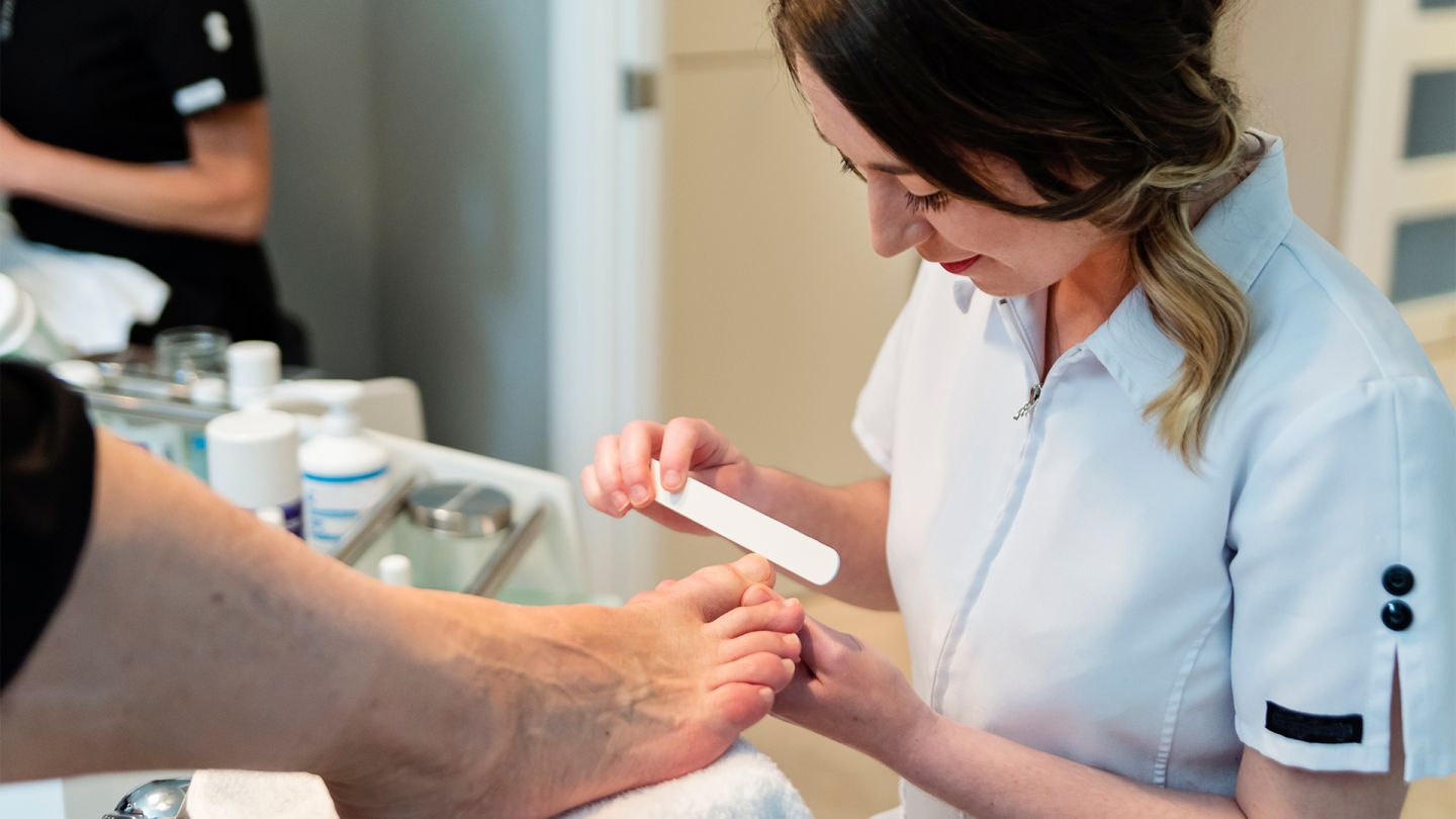 Diabetischer Fuß: Eine junge Dame führt eine Fußpflege durch. Sie feilt die Fußnägel der Person, die gerade behandelt wird.