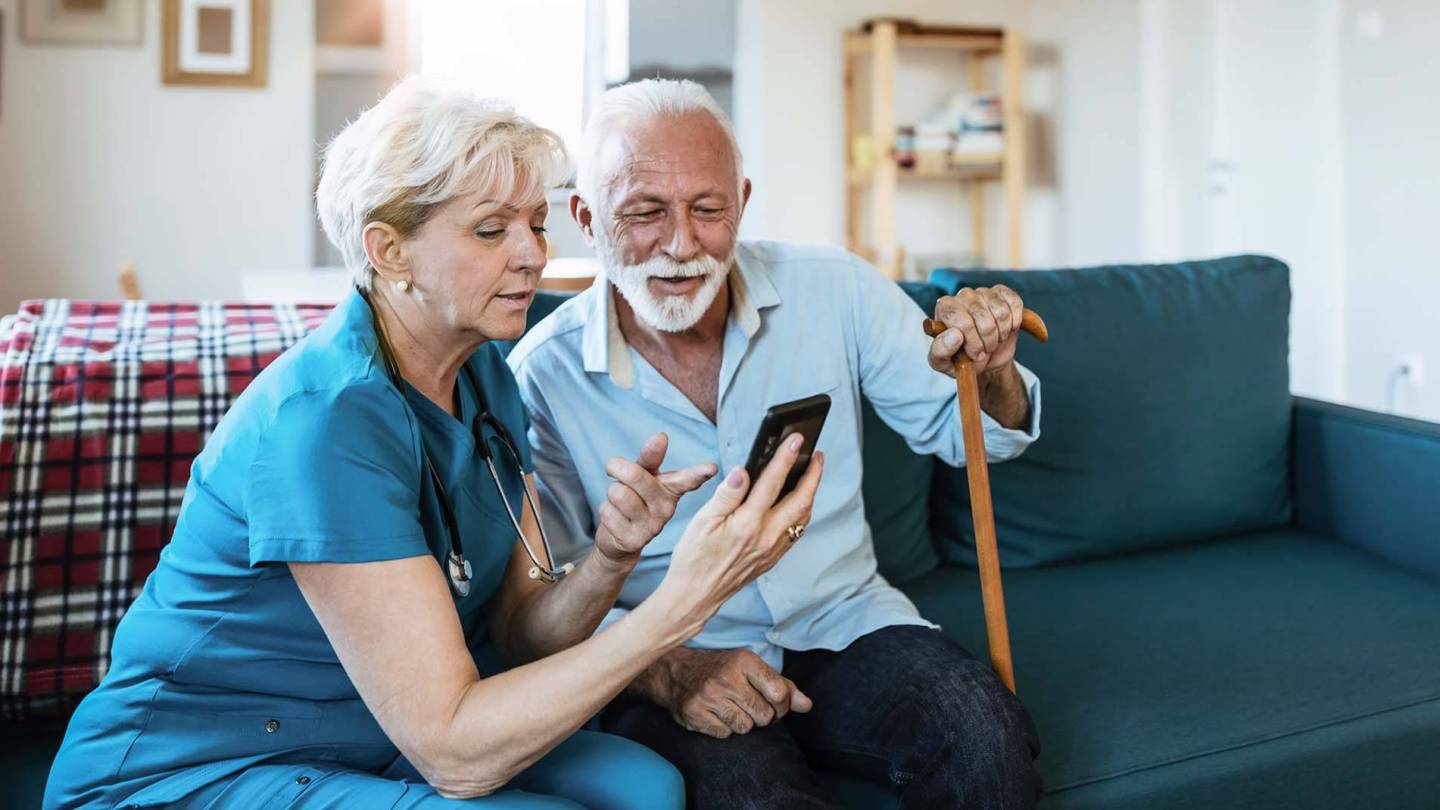 Pflegerin zeigt älterem Mann etwas auf dem Smartphone.