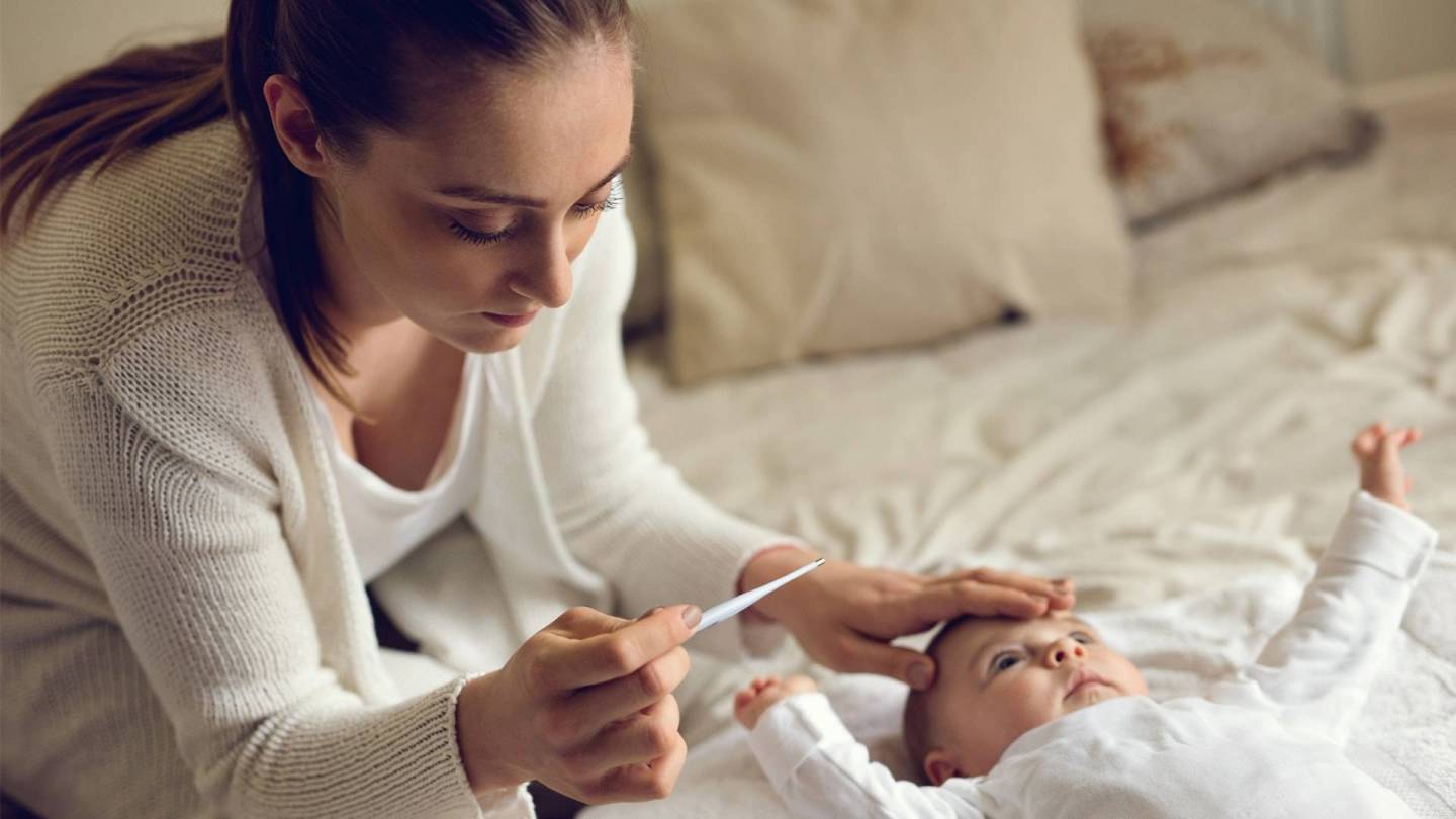 Bir anne bebeğinin alnına dokunuyor ve bir termometreyle ateşinin olup olmadığını kontrol ediyor.