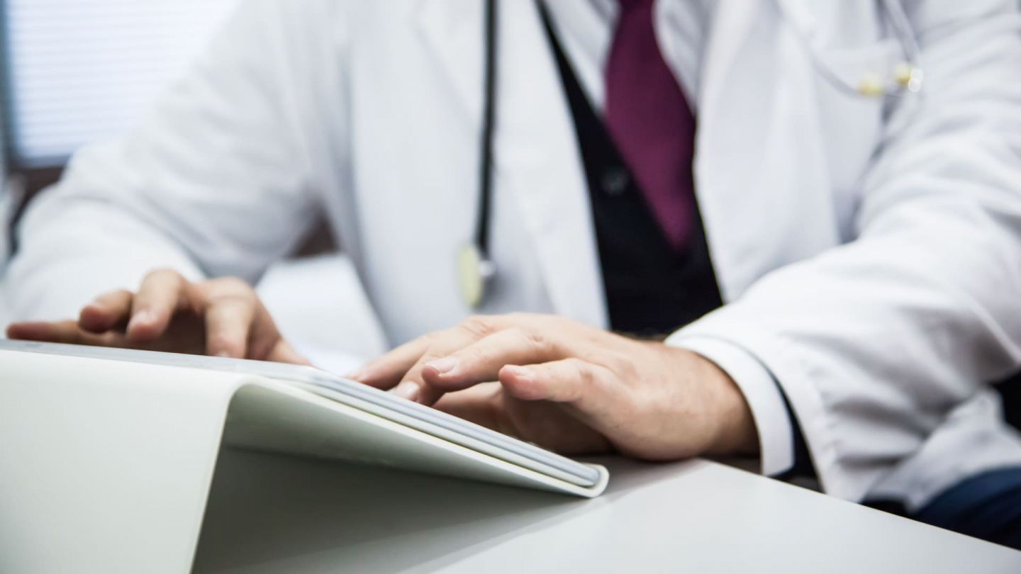 Ein Arzt sitzt am Schreibtisch und tippt etwas auf der Tastatur eines Tablets.