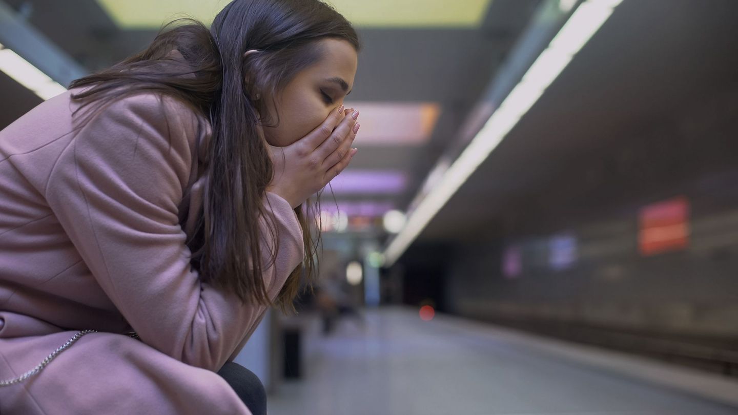 Eine Frau sitzt mit geschlossenen Augen an einer U-Bahn-Haltestelle.