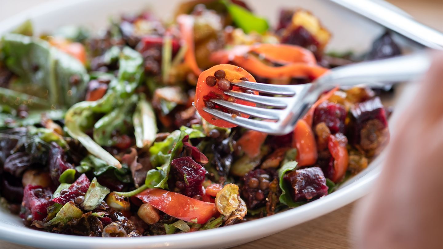 Gesund durch Ernährung: Eine Person piekt mit einer Gabel in einen bunten Salat mit Linsen.