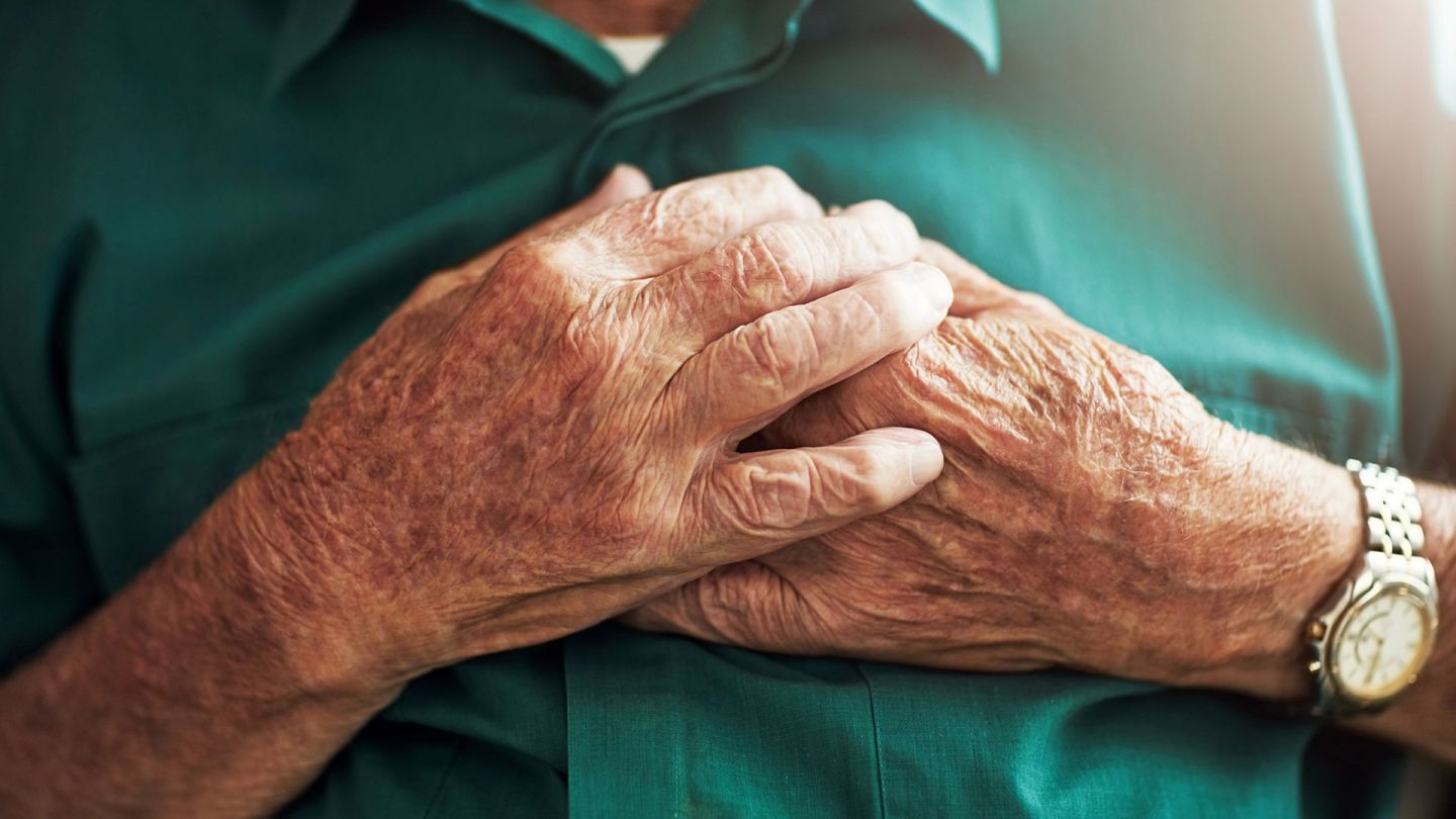Heart attack: older woman holding both hands to her chest.