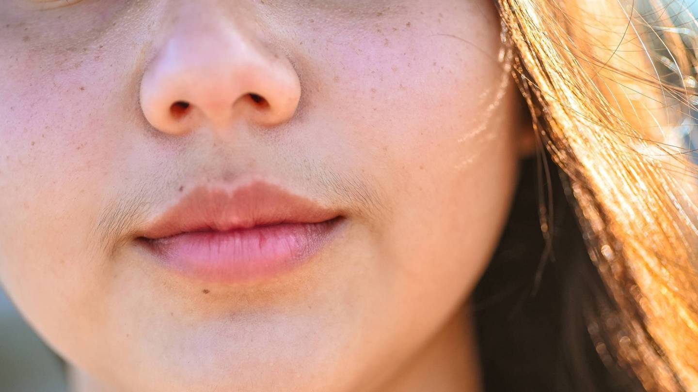 Yakın çekim: Dudak üstü kılları olan genç bir kadının yüzü.
