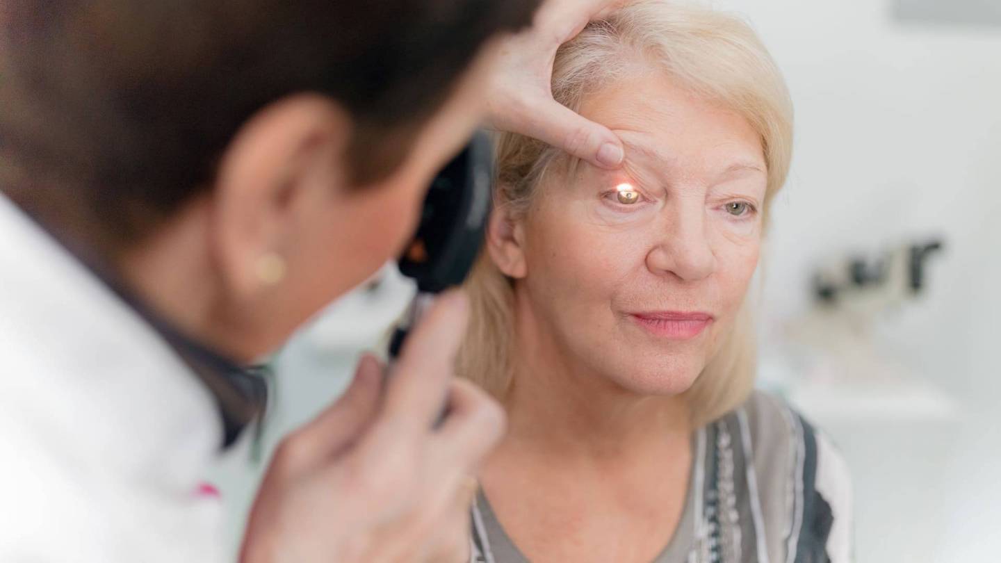 Eine ältere Frau wird untersucht, indem eine Ärztin ihr Augenlid hält und mit einem Messinstrument ins Auge leuchtet.
