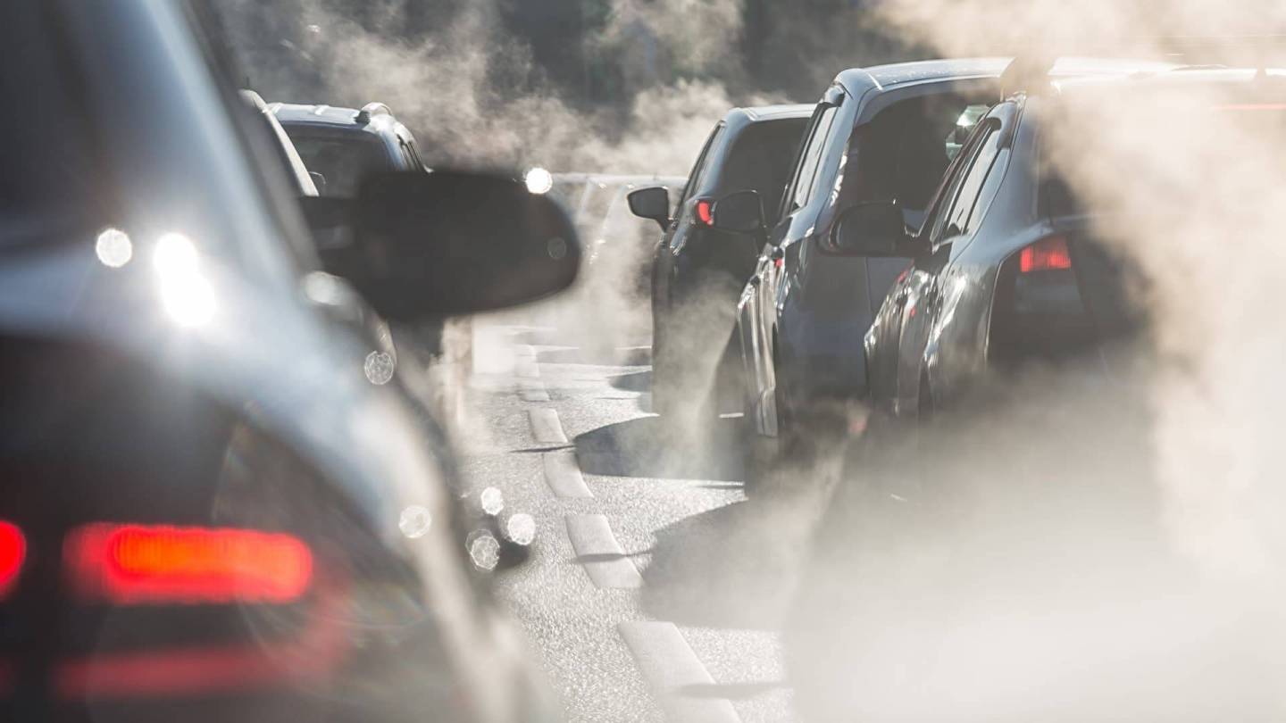 Yavaş ilerleyen trafikteki arabaların ve egzoz gazı bulutlarının yakın çekimi.