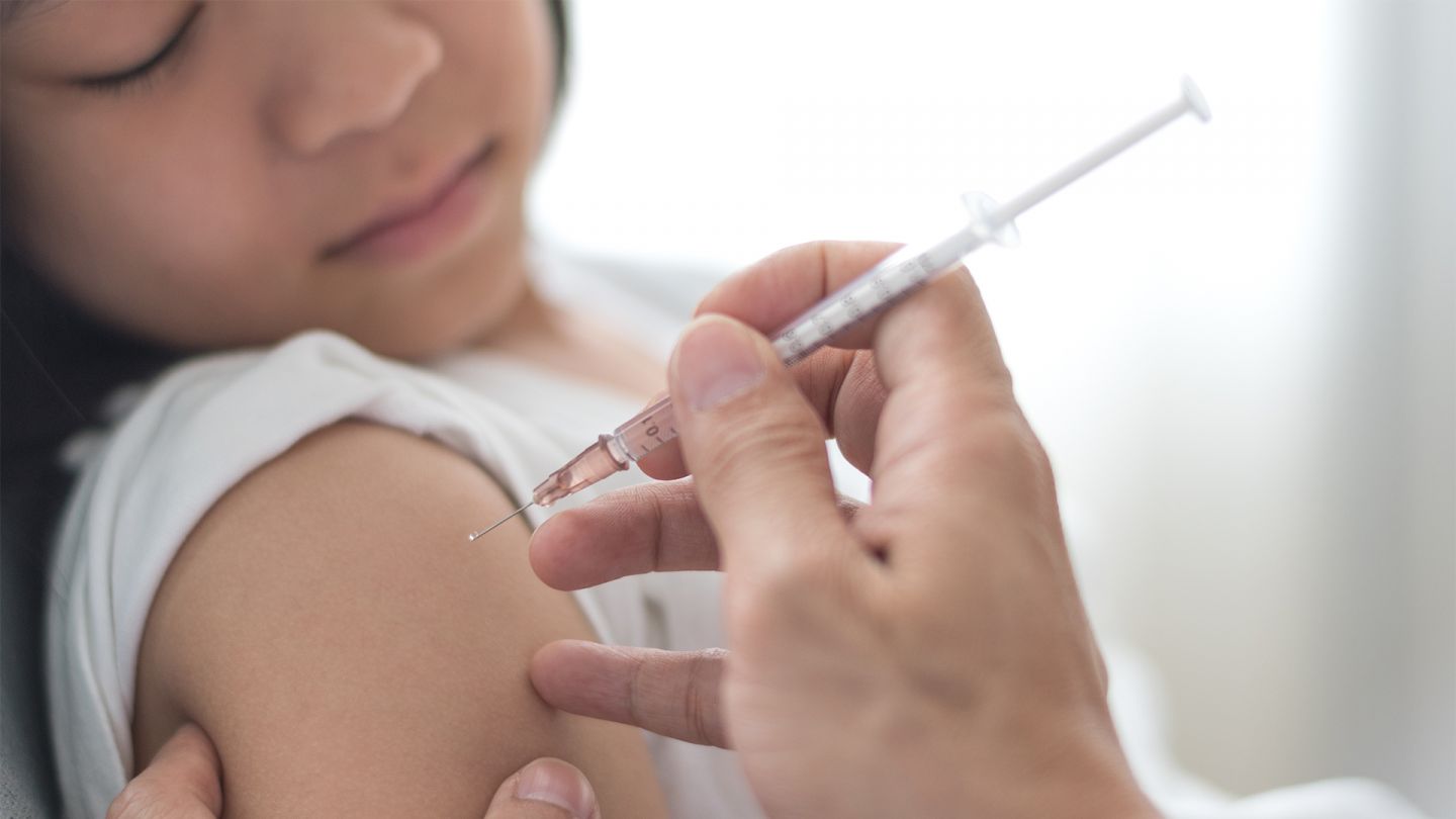 Вакцинация от эпидемического паротита: девочка лежит на кушетке, ей в плечо делают прививку.
