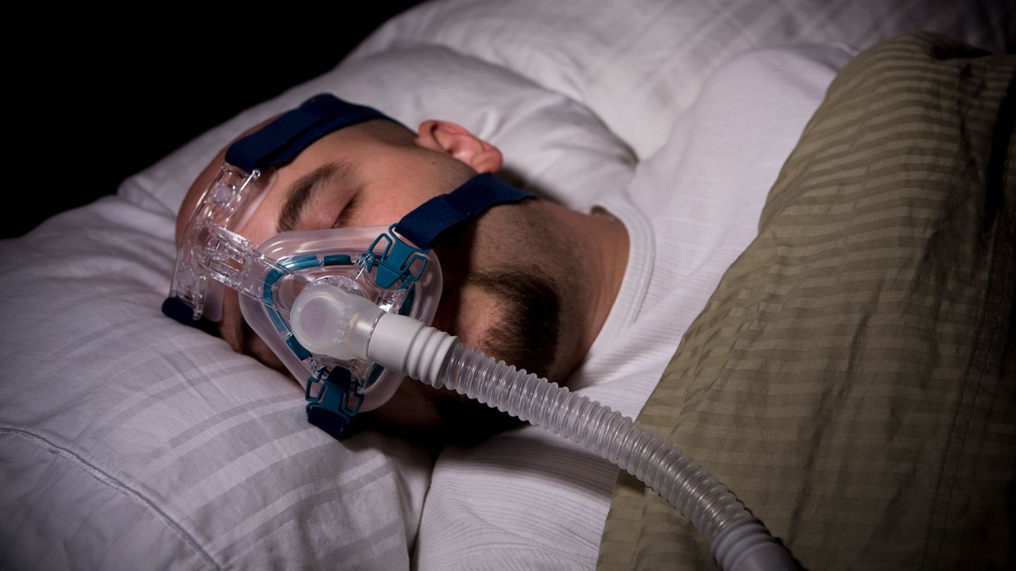 Uyku apnesi: Bir adam yatakta yatıyor ve solunum maskesi takıyor. Uyuyor gibi görünüyor.
