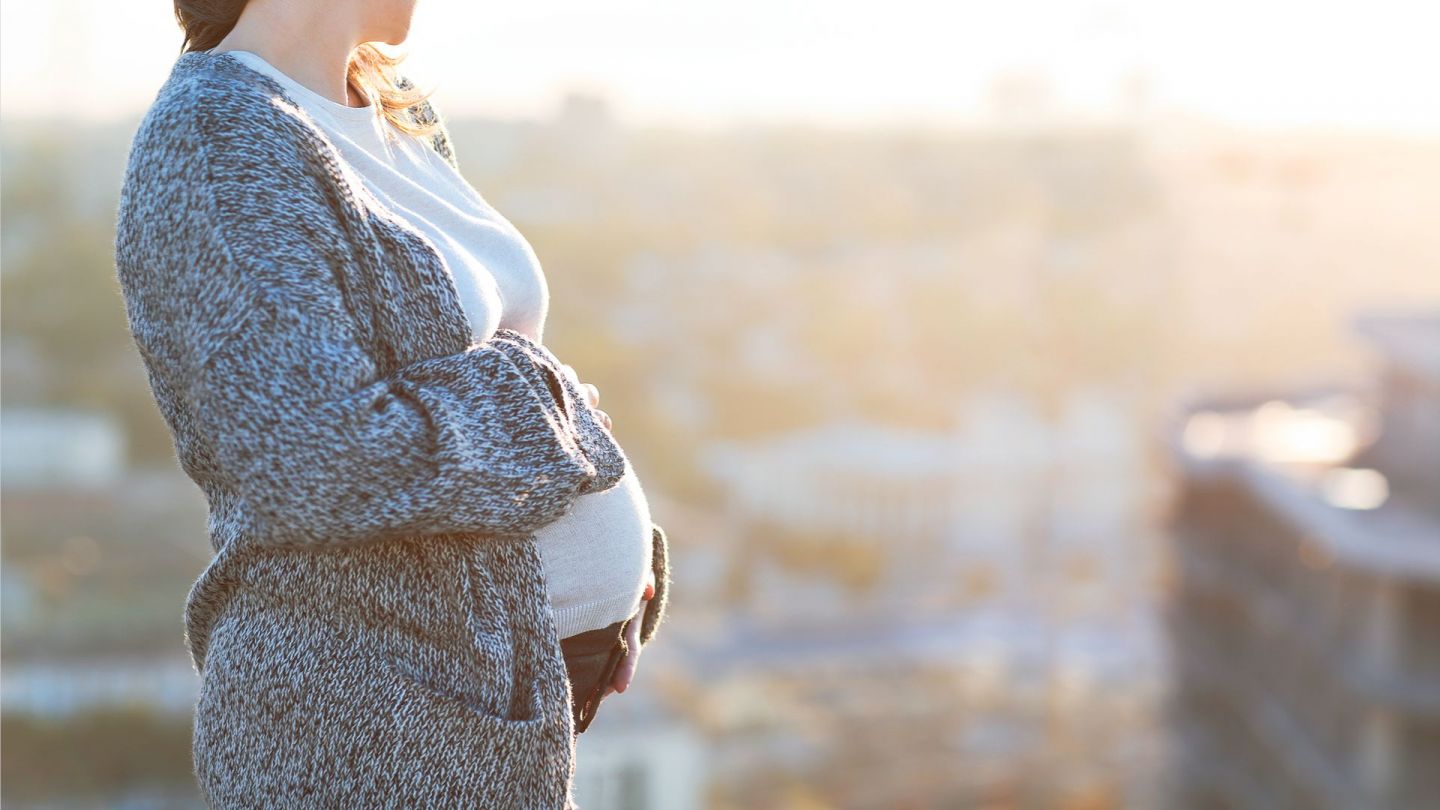 Pregnant woman touching her belly with both hands, cityscape in background.