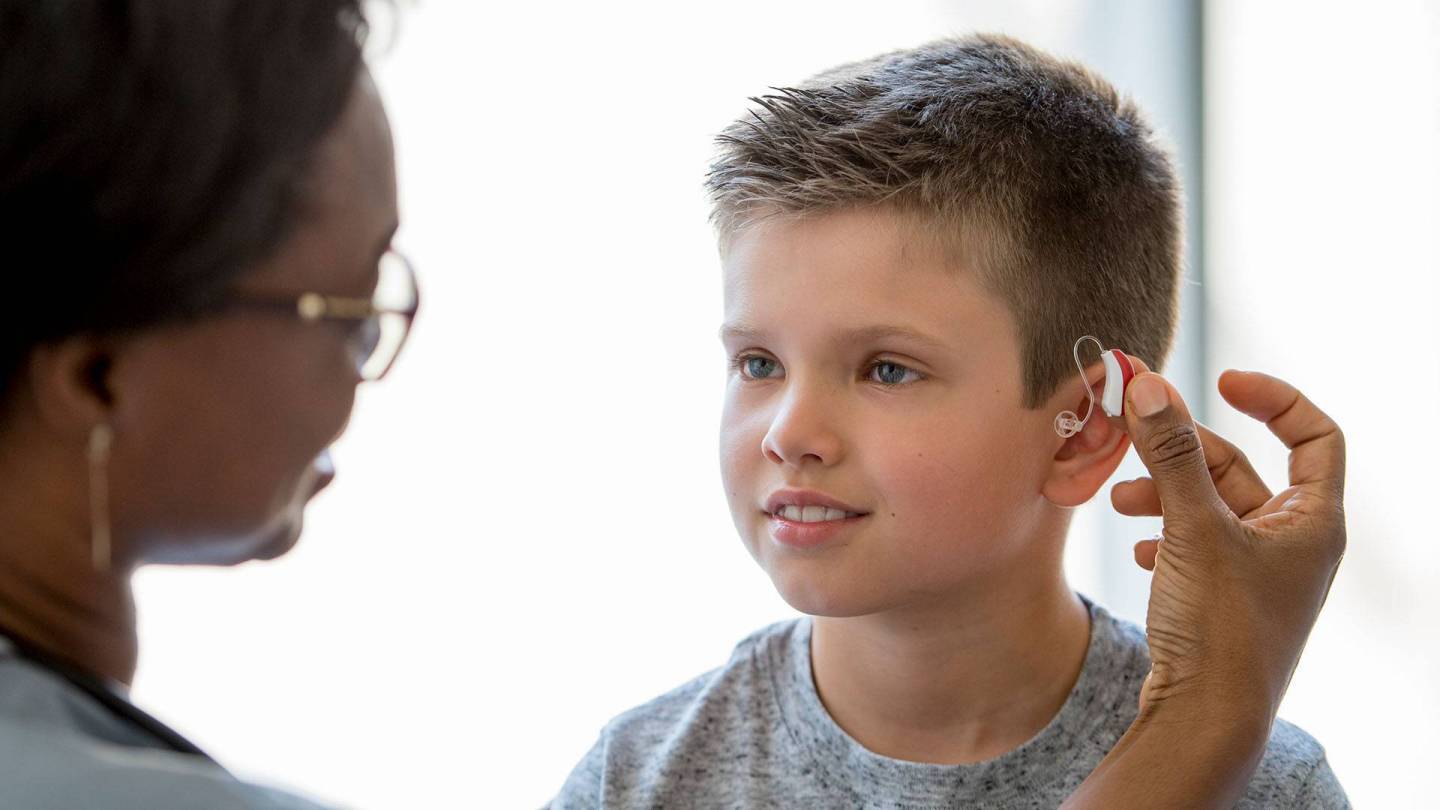 Woman fitting a young boy with a hearing aid.