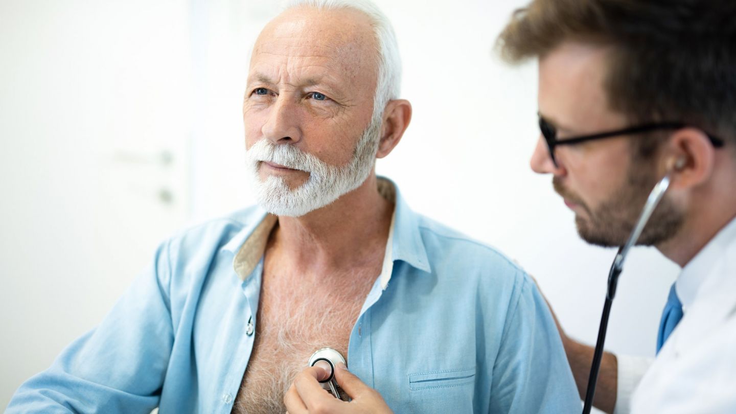 Мужчину в возрасте осматривает врач, он прослушивает сердце пациента с помощью стетоскопа.