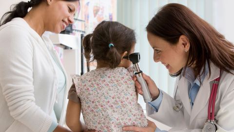Doctor looking into a girl’s ear with an otoscope.