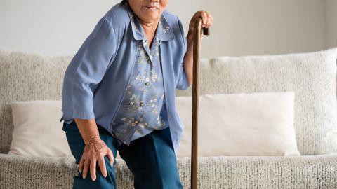 Arthritis: older woman trying to get up from a sofa. She is pulling herself up on a walking stick. She is straining and may be in pain.