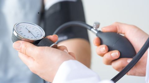 Zwei Hände halten ein Blutdruckmessgerät um den Bluthochdruck eines Patienten zu messen.
