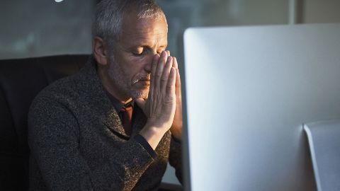 Burnout: man sitting in front of a screen with his eyes closed and his hand on his forehead.