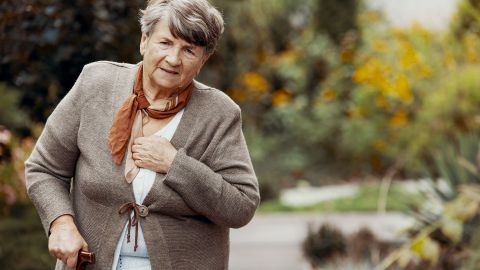 Chronisch-obstruktive Lungenerkrankung: Eine ältere Frau fasst sich an den Brustkorb. In der anderen Hand hält sie einen Gehstock.