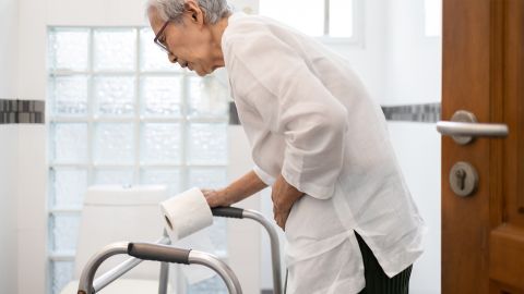Ulcerative colitis: older woman on her way to the toilet. She is leaning on her wheeled walker and clutching her stomach.