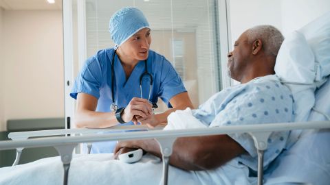 سرطان الأمعاء: طبيب يقف أمام سرير المستشفى وينحني أمام رجل جالس في السرير. وكلا الرجلين ينظران إلى بعضهما.
