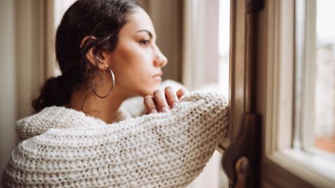 Depression: women looking out of an apartment window lost in thought.