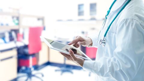 Electronic patient record: doctor standing in a medical practice holding a tablet in his left hand. He is touching the screen with the forefinger of his right hand.