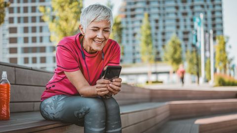 Digital health apps: woman sitting on a wooden bench holding a smartphone in both hands and looking at the screen