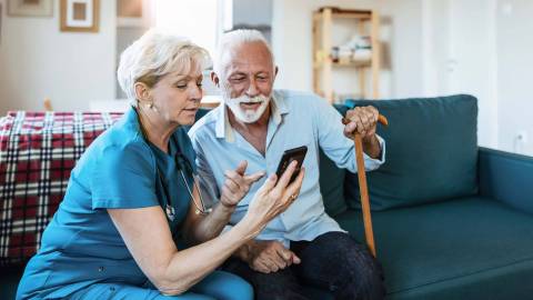 Pflegerin zeigt älterem Mann etwas auf dem Smartphone.