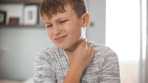 A child touching their sore throat.