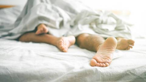 Bare feet of two people in bed sticking out from under a blanket.