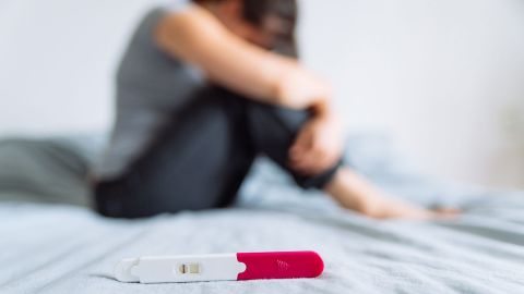 Bir yatakta çömelmiş bir kadın, ayrıca yatakta ön planda negatif bir gebelik testi görülüyor.