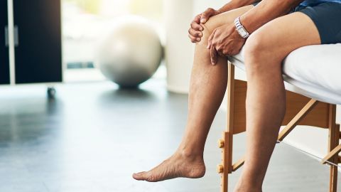 Functional symptoms: man sitting on a chair in a medical examination room holding his knee.