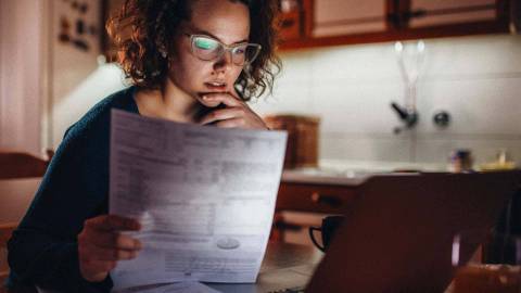 Eine Frau sitzt vor einem Laptop und hält ein Informationsblatt in der Hand.