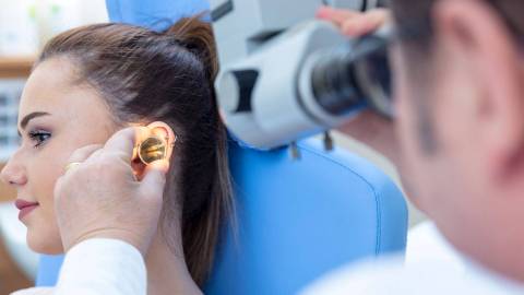 Arzt untersucht das Ohr einer Patientin.