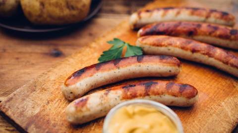 Повышенный уровень холестерина: на деревянной доске лежат свежеприготовленные жареные колбаски.
