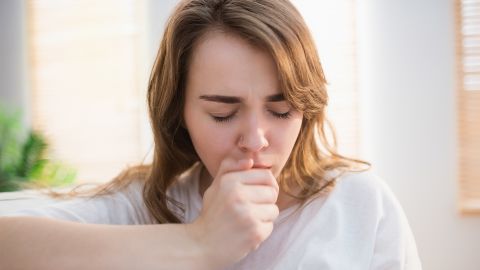 Woman with her eyes closed coughing into her hand.