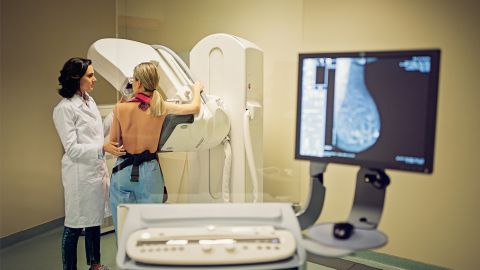 Раннее выявление рака: пациентка проходит маммографический скрининг. Рядом с пациенткой стоит женщина-врач. Она проводит обследование. На экране можно увидеть рентгеновское изображение грудной клетки.