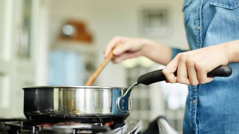Приготовление пищи: сковорода на газовой плите. Кто-то держит сковороду одной рукой и половник другой.