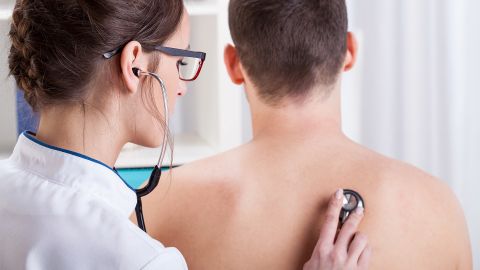 Eine Ärztin hält ein Stethoskop an den nackten Rücken eines Mannes.