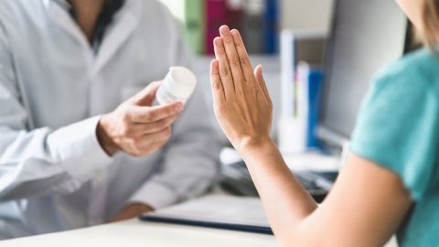 Medikamentenallergie: Ein Arzt hält ein Medikament in der Hand, zeigt es einer Frau. Sie hebt abwehrend die Hand, sie scheint eine Medikamentenallergie zu haben.