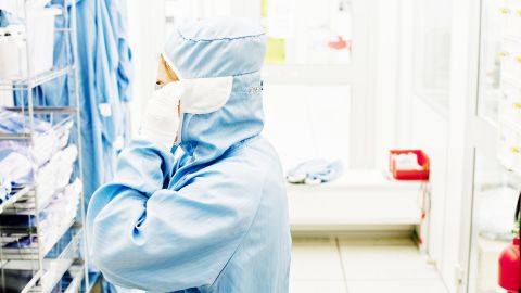 الجمرة الخبيثة: شخص يرتدي بدلة واقية تغطيه من الرأس إلى إخمص القدمين ويقف أمام رف في المختبر.