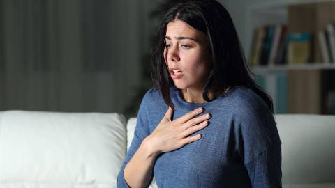 Eine Frau hält ihre flache Hand auf der Brust, sie ist verkrampft und unter akuter Atemnot.