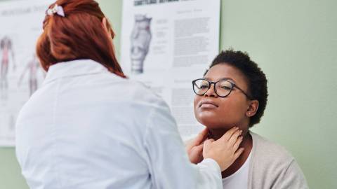 Женщина-врач проводит обследование лимфатических узлов на шее молодой пациентки.