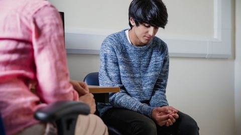 Phimose: Ein Jugendlicher sitzt auf einem Stuhl in einem Behandlungszimmer. Seine Hände liegen in seinem Schoß, er wirkt bedrückt.