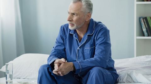Benign prostate enlargement (benign prostatic hyperplasia): middle-age man sitting on the edge of a hospital bed. He has his hands entwined and is looking thoughtfully out of the window.